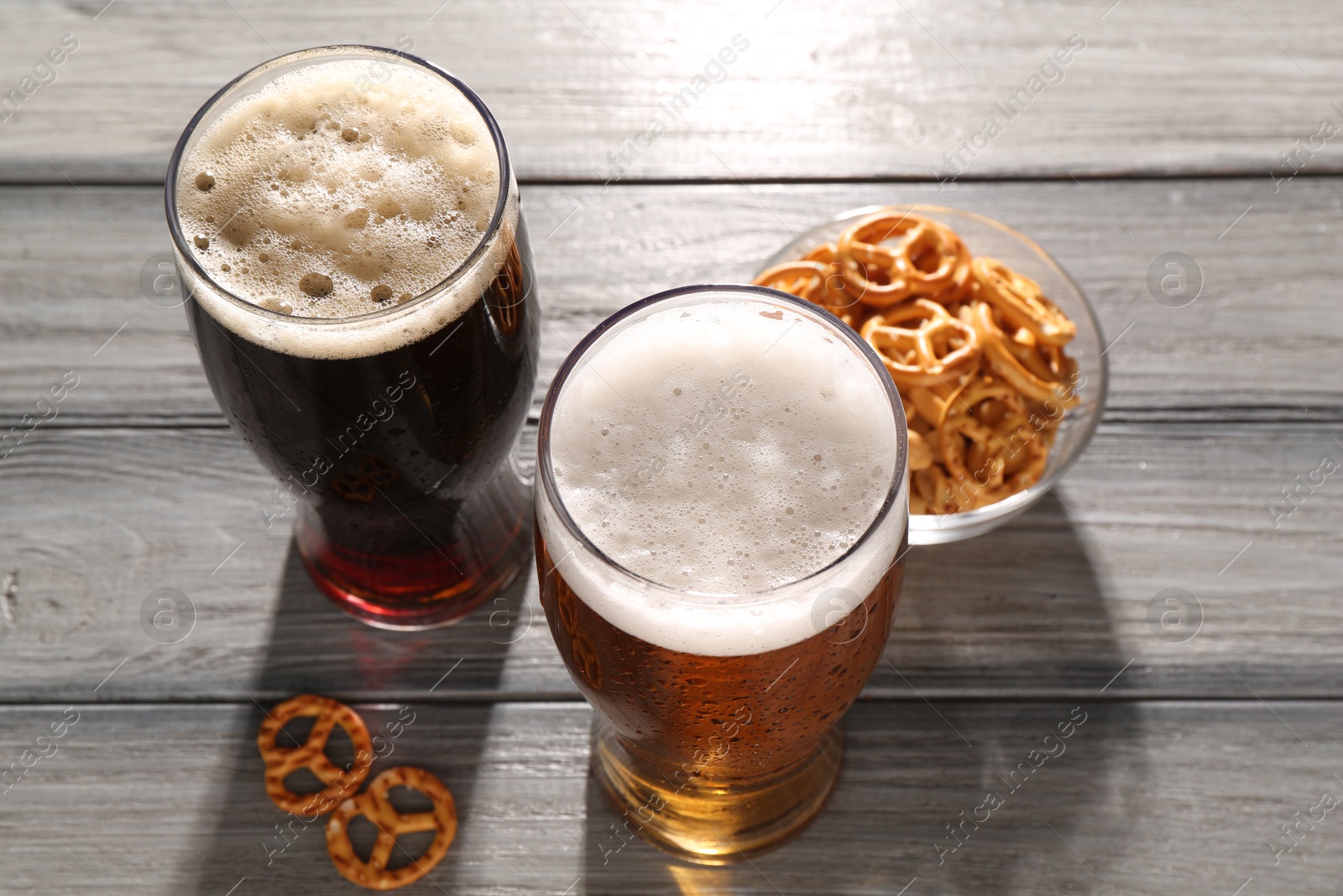 Photo of Glasses of beer and pretzel crackers on grey wooden table, above view