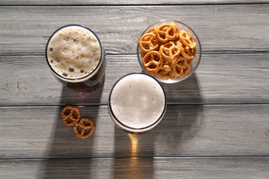 Glasses of beer and pretzel crackers on grey wooden table, flat lay