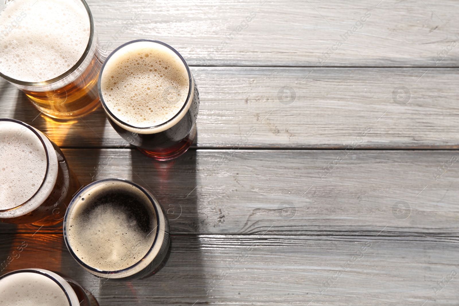 Photo of Glasses with different types of beer on grey wooden table, flat lay. Space for text