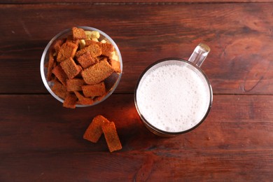 Photo of Glass mug of beer and rusks on wooden table, flat lay