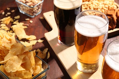 Glasses of beer and snacks on wooden table, closeup