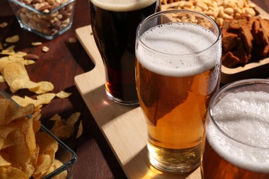 Glasses of beer and snacks on wooden table, closeup