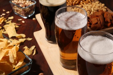 Glasses of beer and snacks on wooden table, closeup