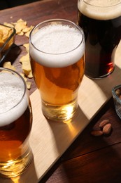 Glasses of beer and snacks on wooden table, closeup
