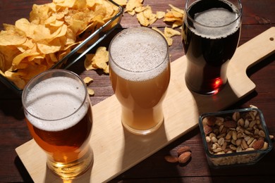 Glasses of beer and snacks on wooden table