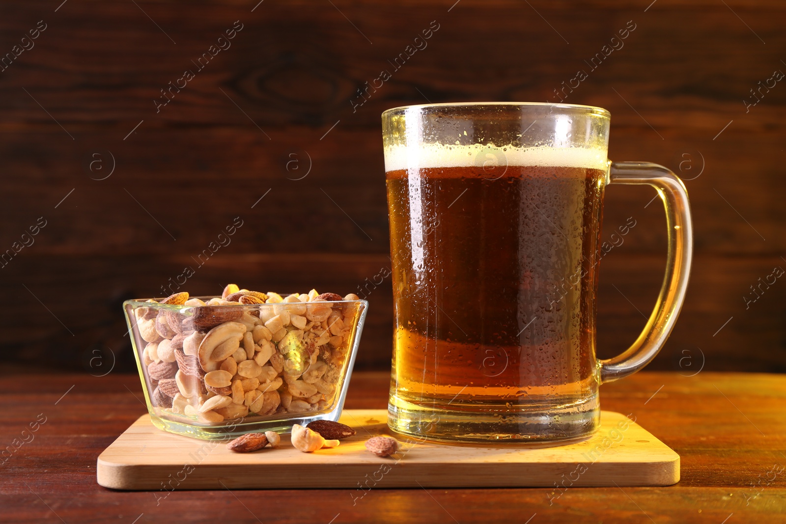 Photo of Glass mug of beer and nuts on wooden table