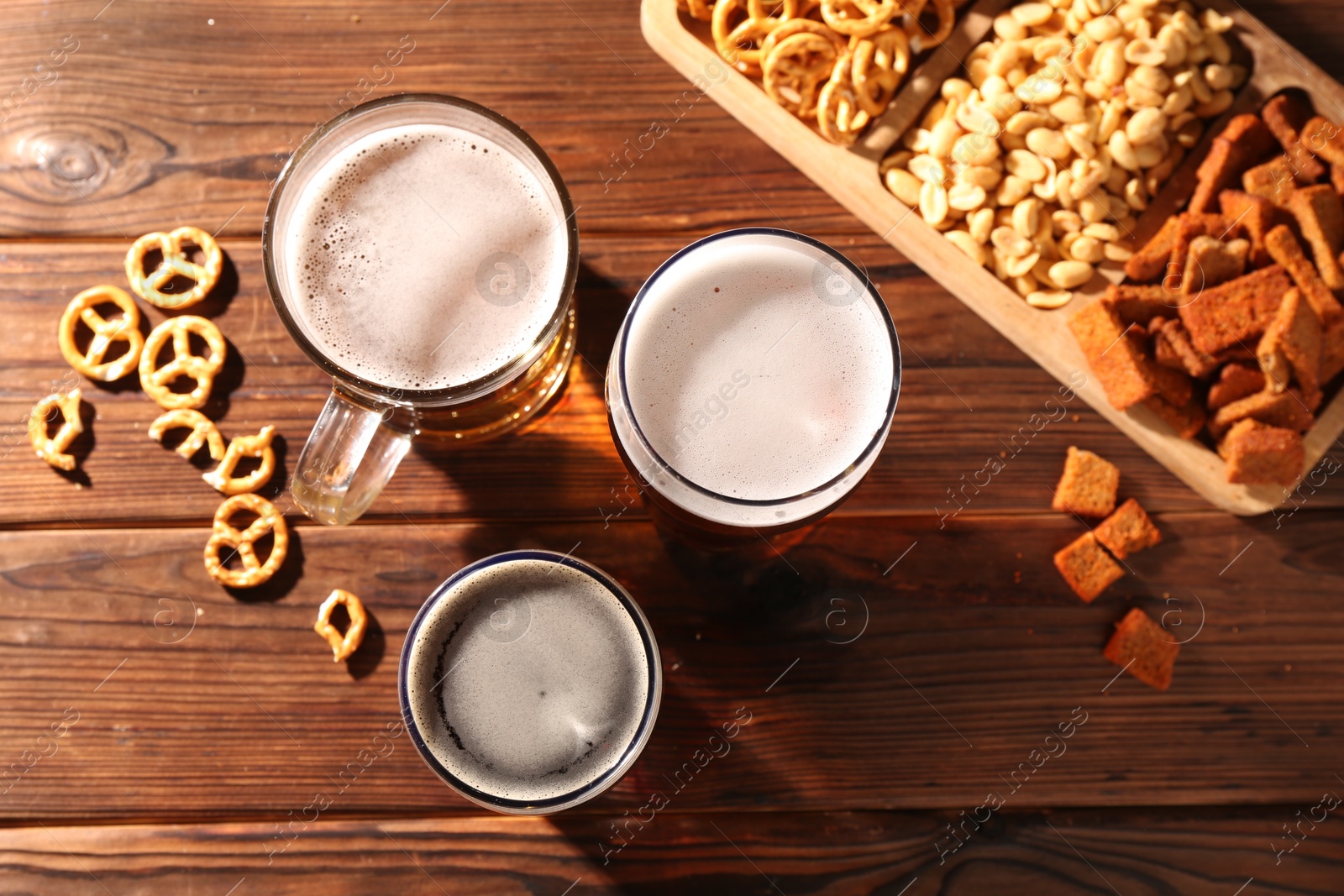 Photo of Glasses with different types of beer and snacks on wooden table, flat lay