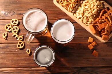 Photo of Glasses with different types of beer and snacks on wooden table, flat lay