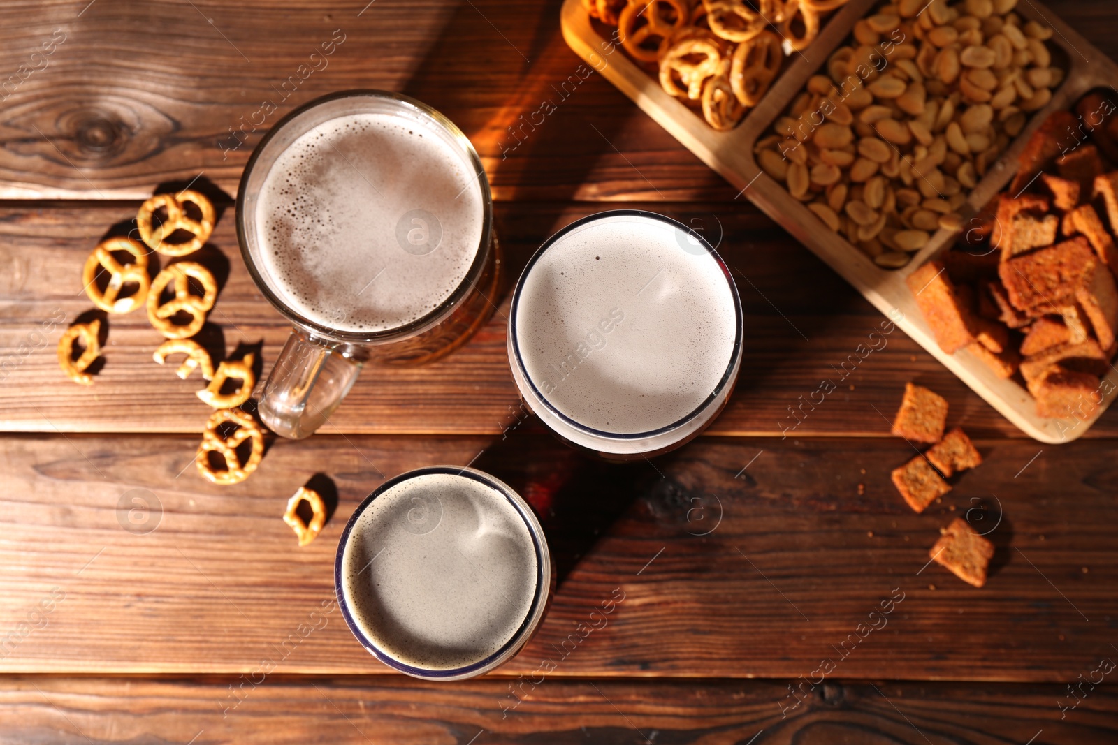 Photo of Glasses with different types of beer and snacks on wooden table, flat lay