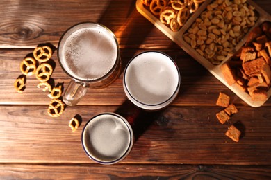 Photo of Glasses with different types of beer and snacks on wooden table, flat lay