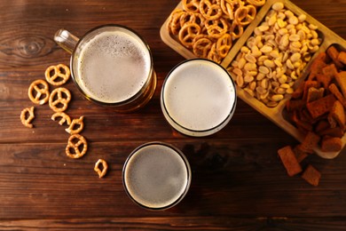 Photo of Glasses with different types of beer and snacks on wooden table, flat lay