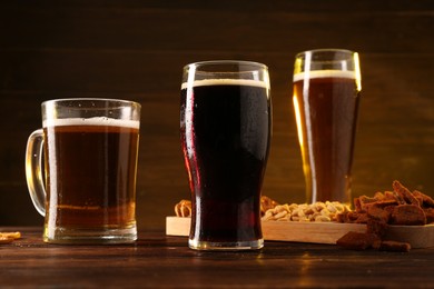 Glasses with different types of beer and snacks on wooden table