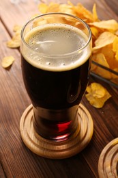 Glass of beer and potato chips on wooden table, closeup