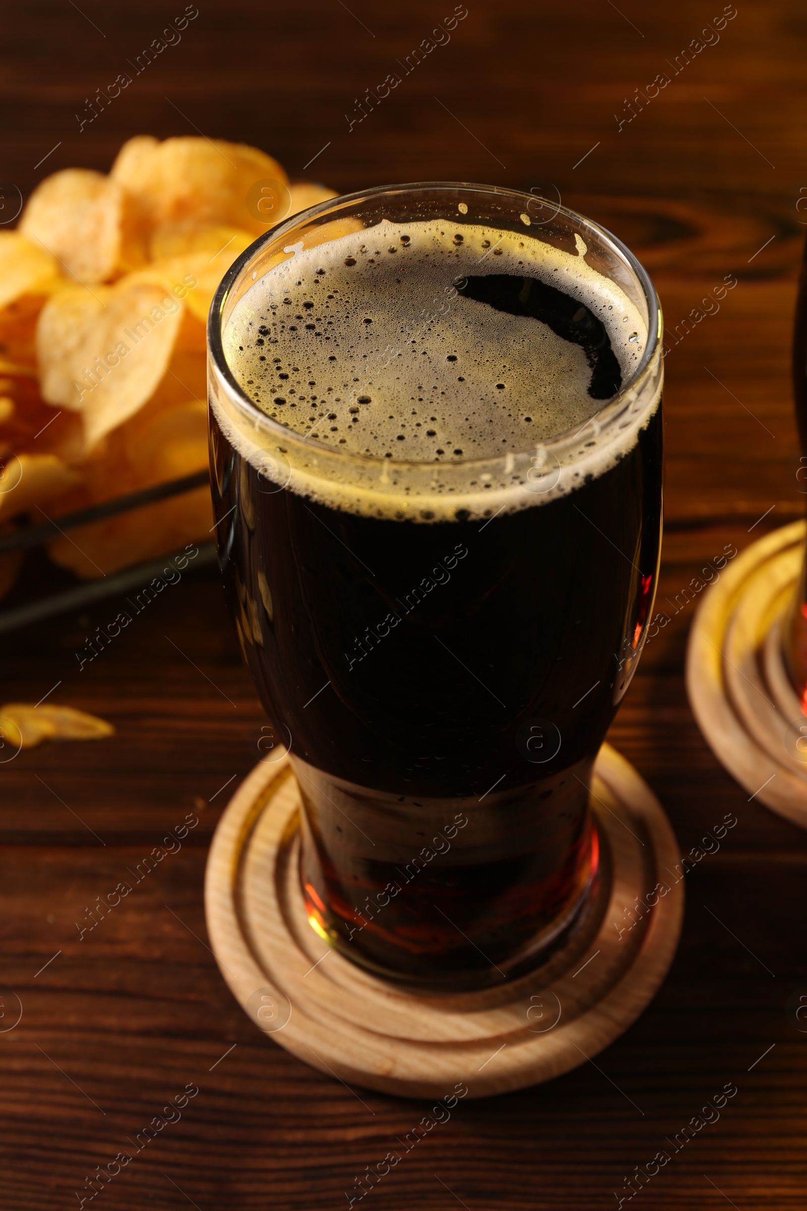 Photo of Glass of beer and potato chips on wooden table, closeup