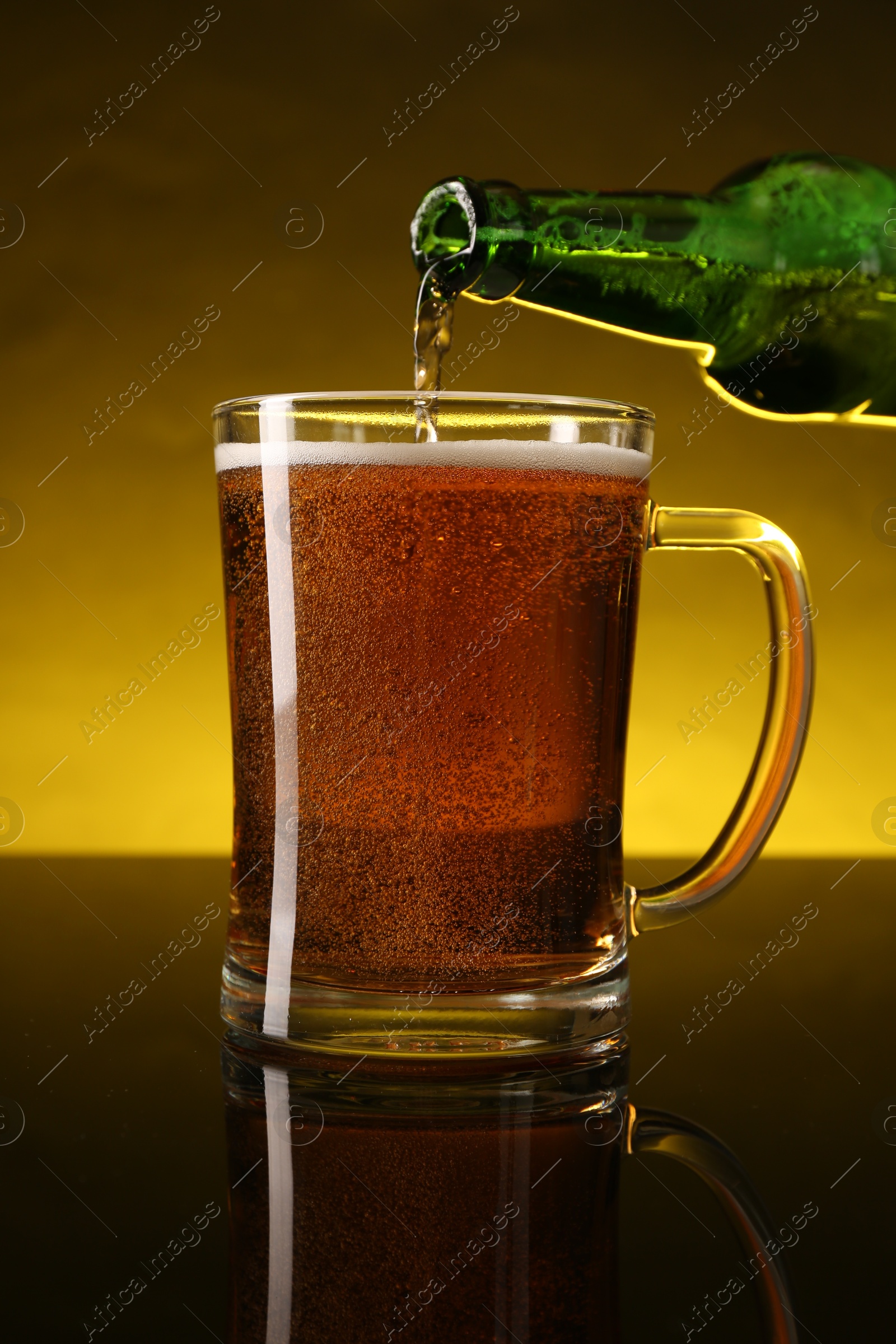 Photo of Pouring beer into glass mug from bottle on dark table, closeup