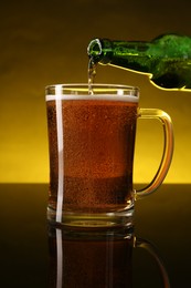 Photo of Pouring beer into glass mug from bottle on dark table, closeup