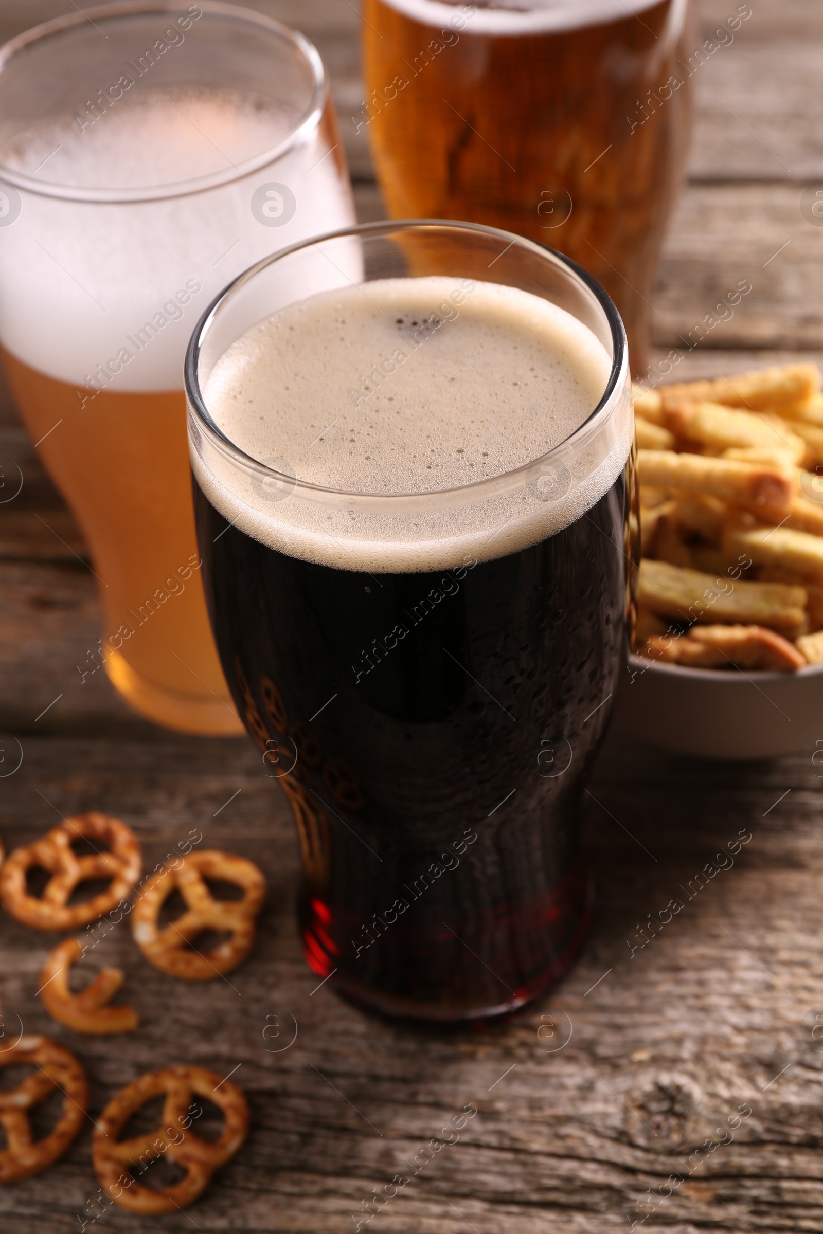 Photo of Glasses of beer, pretzel crackers and rusks on wooden table, closeup
