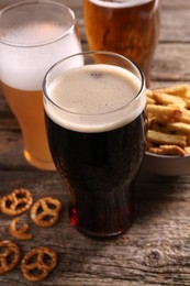 Glasses of beer, pretzel crackers and rusks on wooden table, closeup