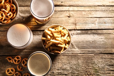 Photo of Glasses of beer, pretzel crackers and rusks on wooden table, flat lay. Space for text