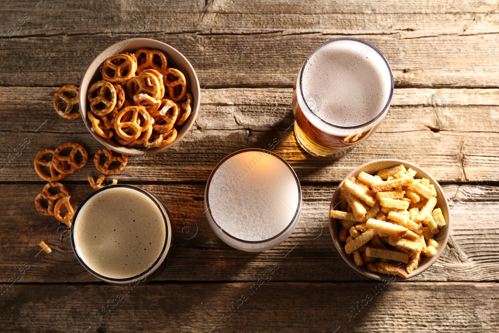 Photo of Glasses of beer, pretzel crackers and rusks on wooden table, flat lay