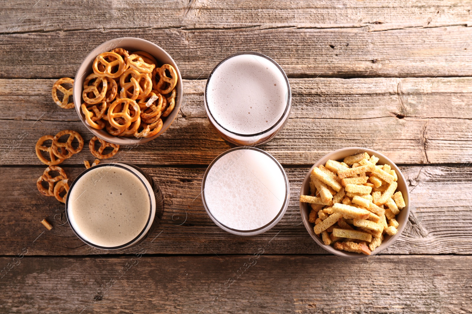 Photo of Glasses of beer, pretzel crackers and rusks on wooden table, flat lay