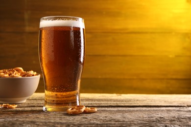 Photo of Glass of beer and pretzel crackers on wooden table, space for text