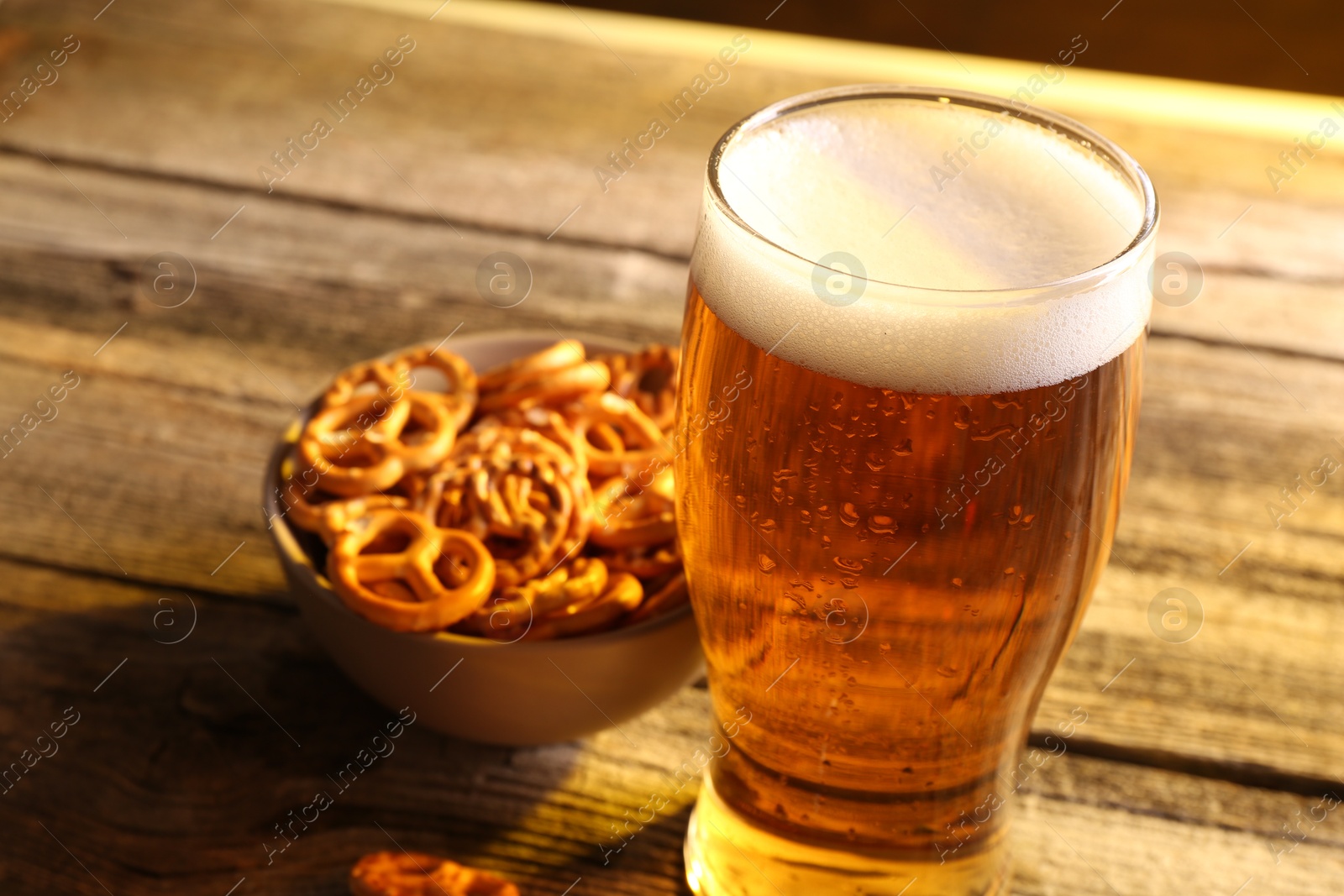 Photo of Glass of beer and pretzel crackers on wooden table, closeup