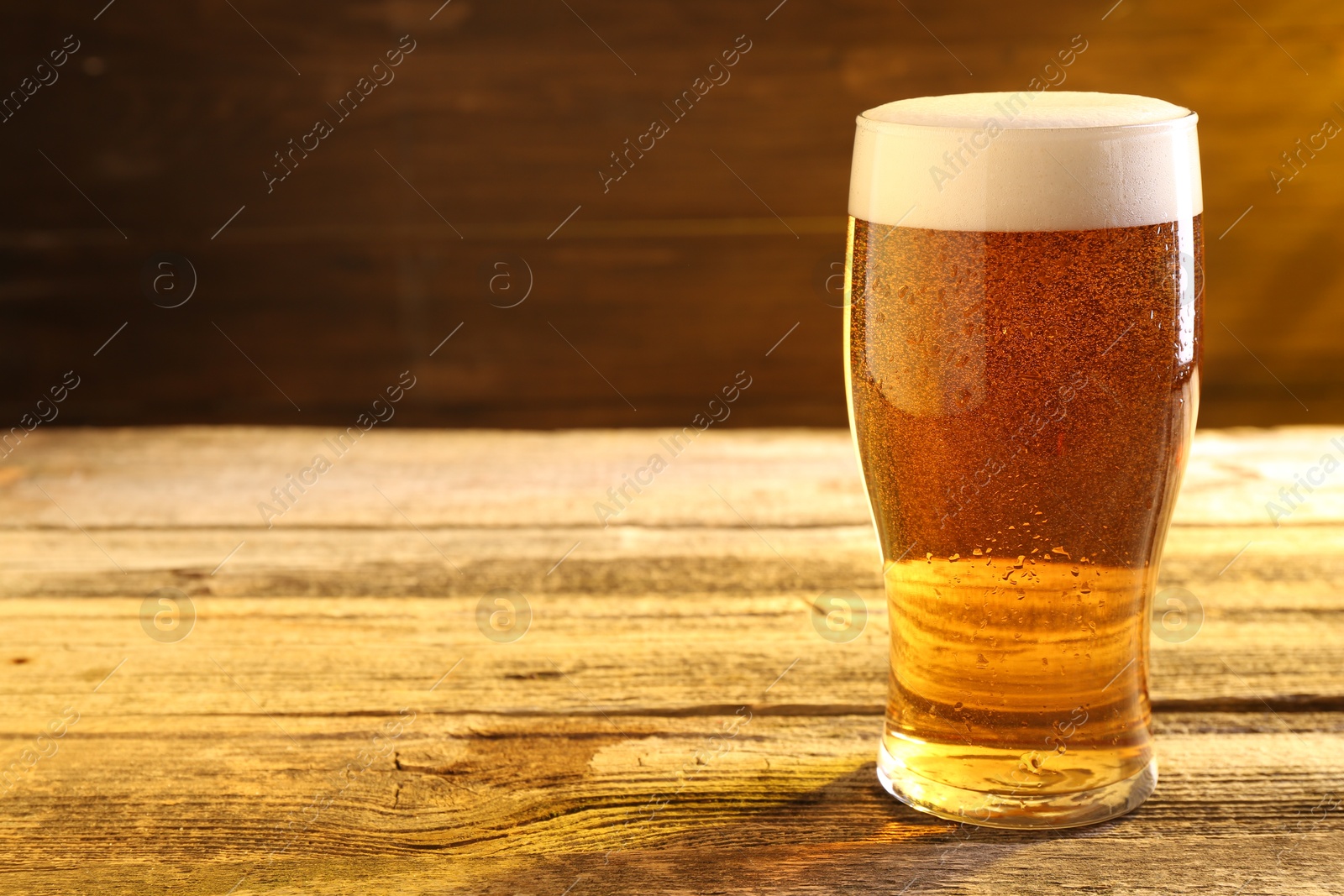 Photo of Glass of beer on wooden table, space for text