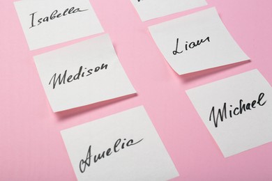 Photo of Paper stickers with different names on pink background, closeup. Choosing baby's name