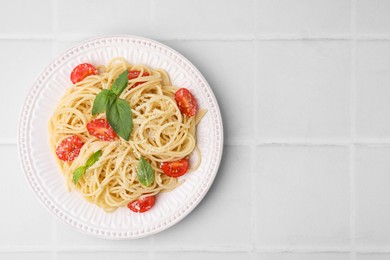 Photo of Tasty pasta with tomato, cheese and basil on white tiled table, top view. Space for text