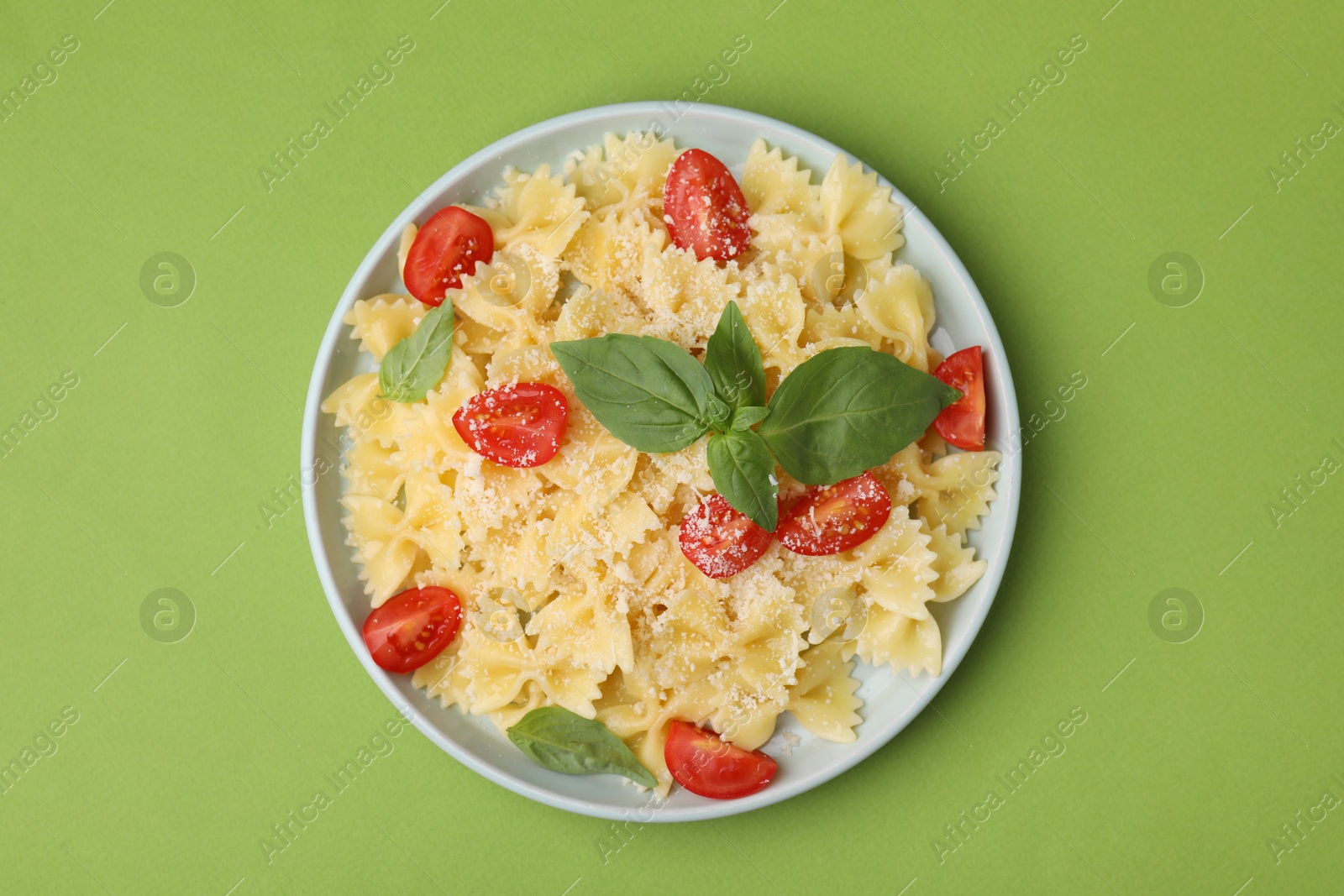 Photo of Tasty pasta with tomato, cheese and basil on green table, top view