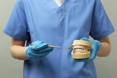Doctor holding dental model with jaws and tool on grey background, closeup. Cast of teeth
