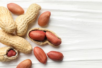 Fresh unpeeled peanuts on white wooden table, flat lay. Space for text