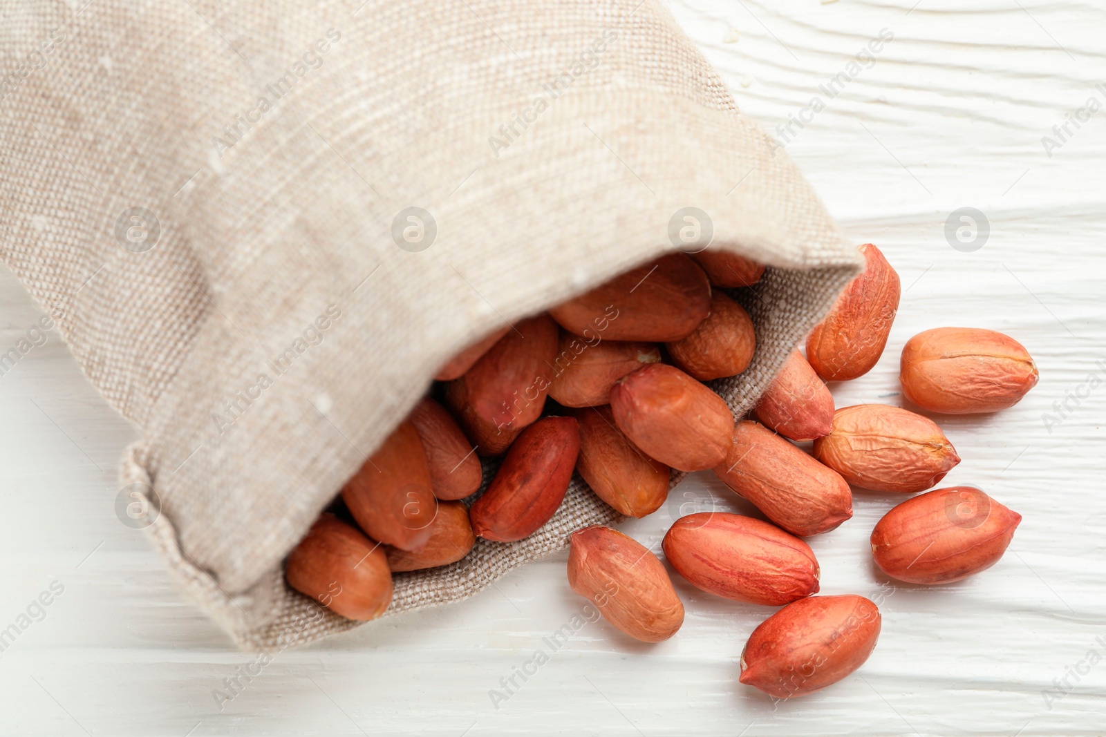 Photo of Fresh peanuts in sack on white wooden table, above view