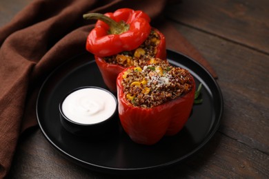 Photo of Quinoa stuffed peppers with corn and sauce on wooden table