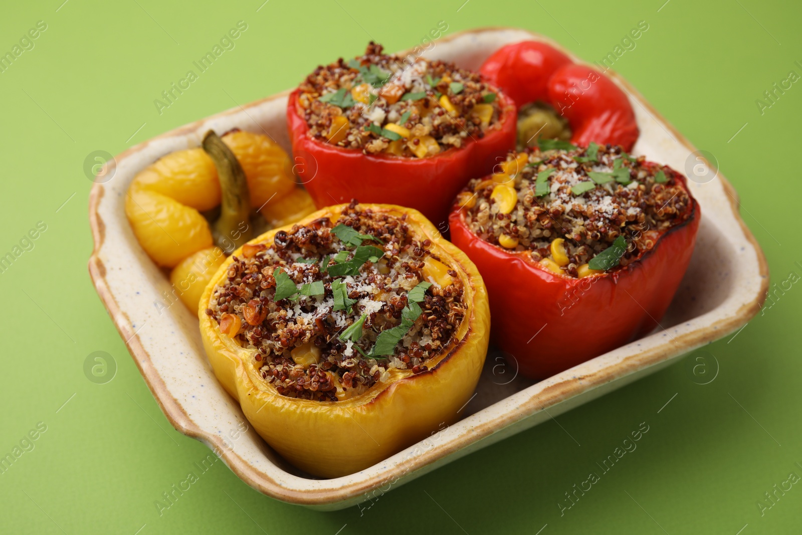 Photo of Tasty quinoa stuffed bell peppers with corn in baking dish on light green table