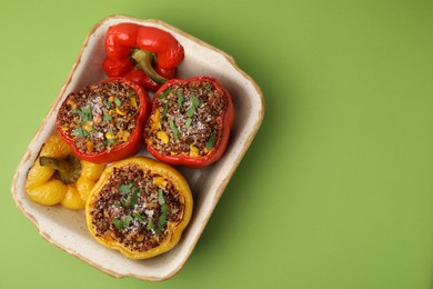 Photo of Tasty quinoa stuffed bell peppers with corn in baking dish on light green table, top view. Space for text