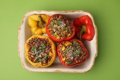 Photo of Tasty quinoa stuffed bell peppers with corn in baking dish on light green table, top view