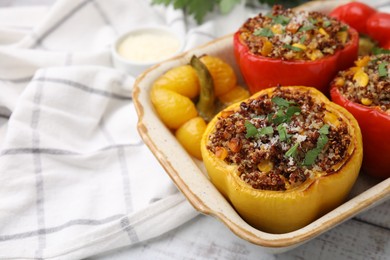 Photo of Tasty quinoa stuffed bell peppers with corn in baking dish on white wooden table, closeup. Space for text