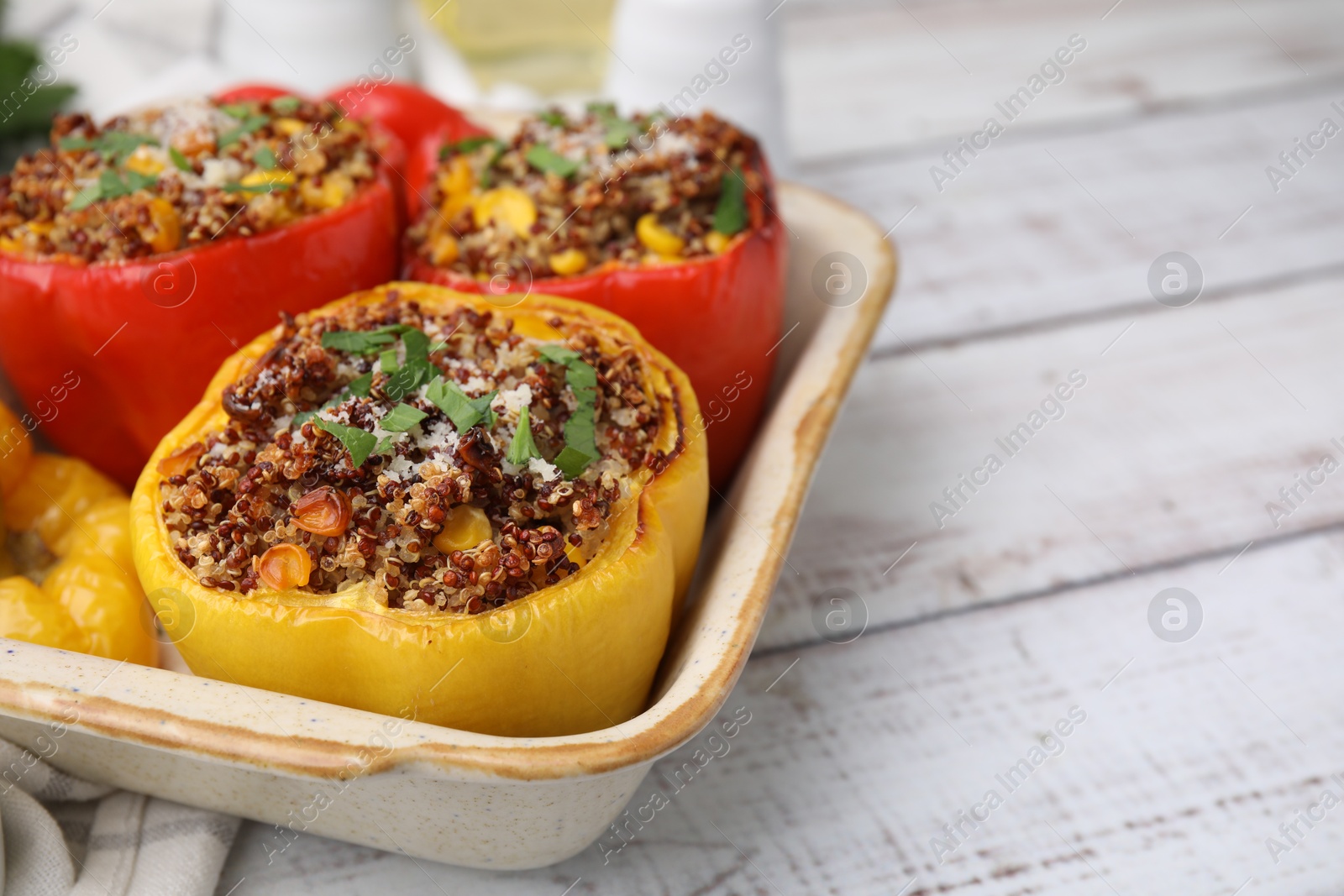 Photo of Tasty quinoa stuffed bell peppers with corn in baking dish on white wooden table, closeup. Space for text