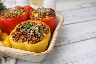 Photo of Tasty quinoa stuffed bell peppers with corn in baking dish on white wooden table, closeup. Space for text