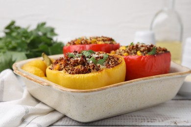 Photo of Tasty quinoa stuffed bell peppers with corn in baking dish on white wooden table, closeup