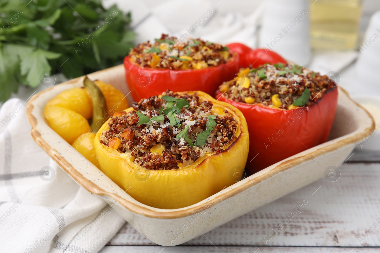 Photo of Tasty quinoa stuffed bell peppers with corn in baking dish on white wooden table, closeup