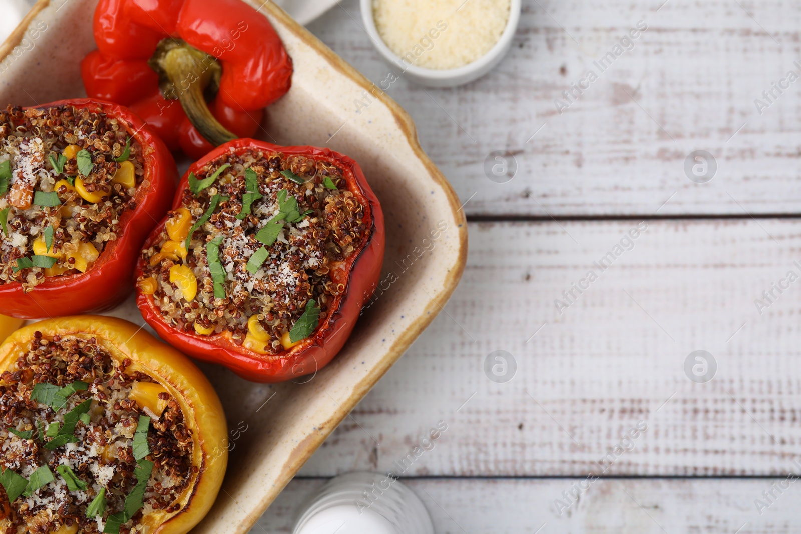 Photo of Tasty quinoa stuffed bell peppers with corn in baking dish on white wooden table, flat lay. Space for text