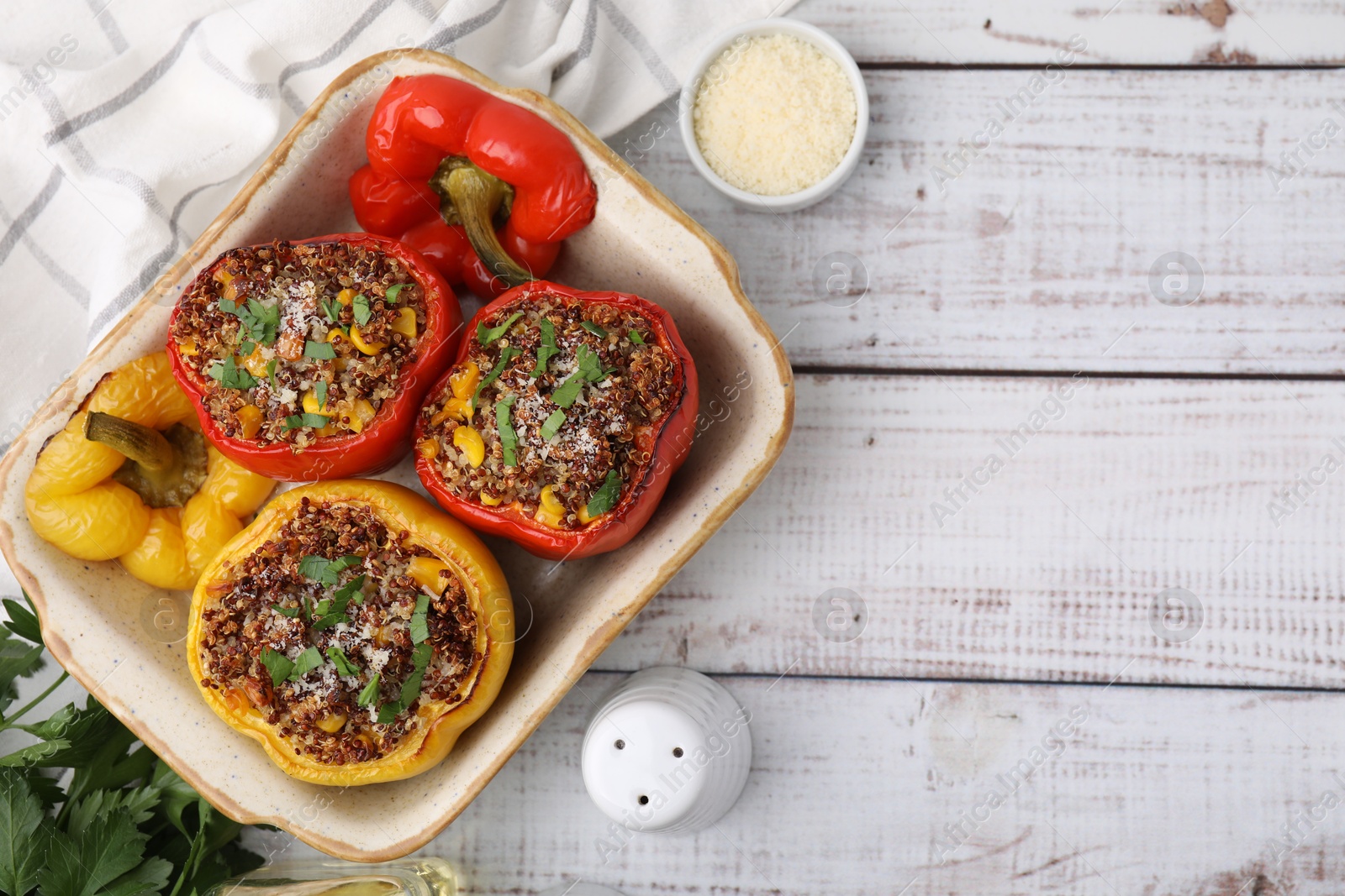 Photo of Tasty quinoa stuffed bell peppers with corn in baking dish on white wooden table, flat lay. Space for text