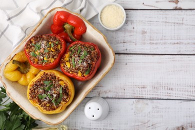 Photo of Tasty quinoa stuffed bell peppers with corn in baking dish on white wooden table, flat lay. Space for text