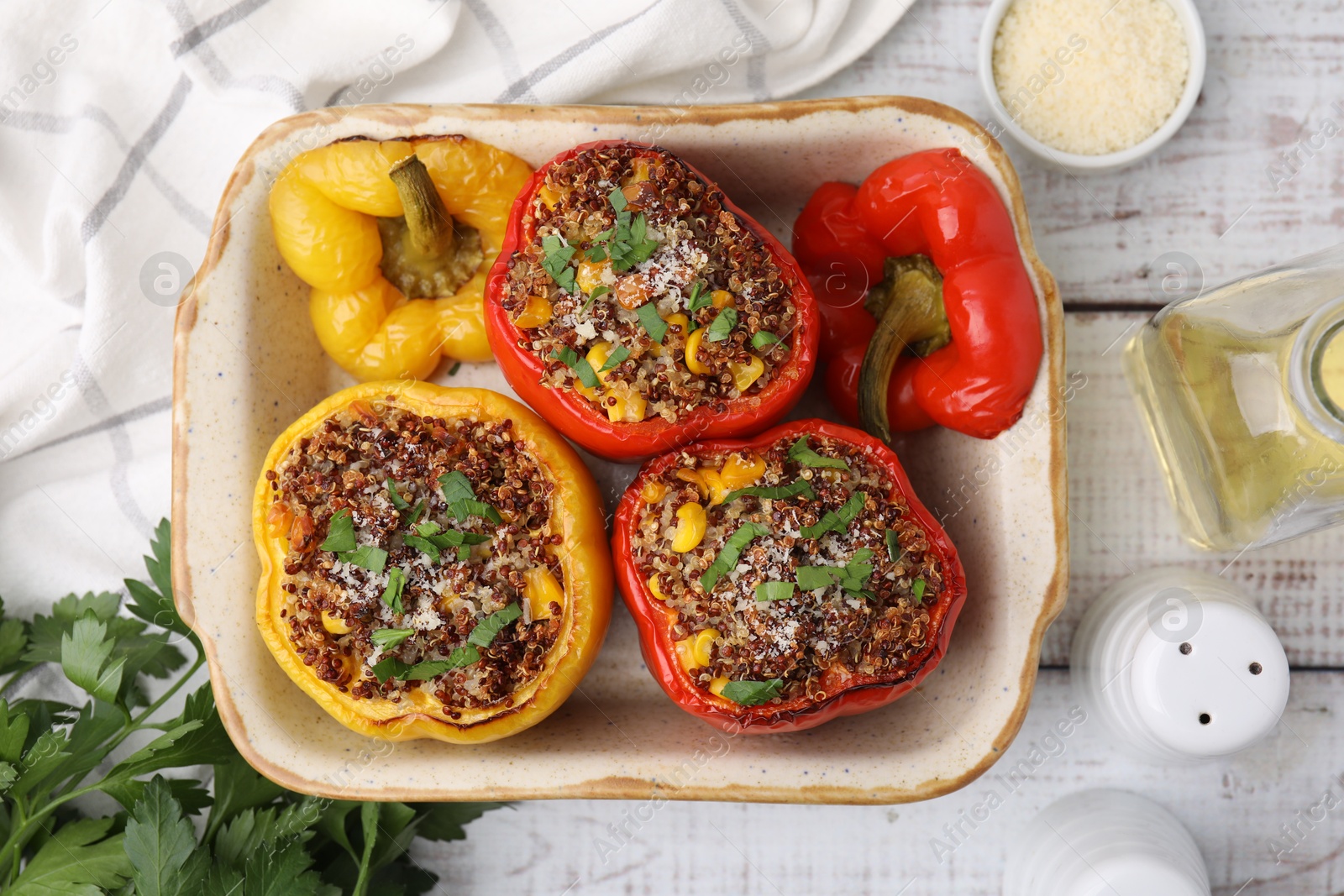 Photo of Tasty quinoa stuffed bell peppers with corn in baking dish on white wooden table, flat lay