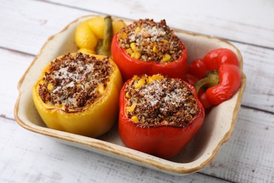 Photo of Tasty quinoa stuffed bell peppers with corn in baking dish on white wooden table