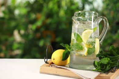 Photo of Refreshing lemonade with mint in jug and citrus fruit on light table against blurred green background. Space for text