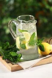 Refreshing lemonade with mint in jug and citrus fruit on light table against blurred green background